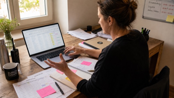 Eventkoordinatorin vergleicht Schichtpläne auf Laptop und Notizen